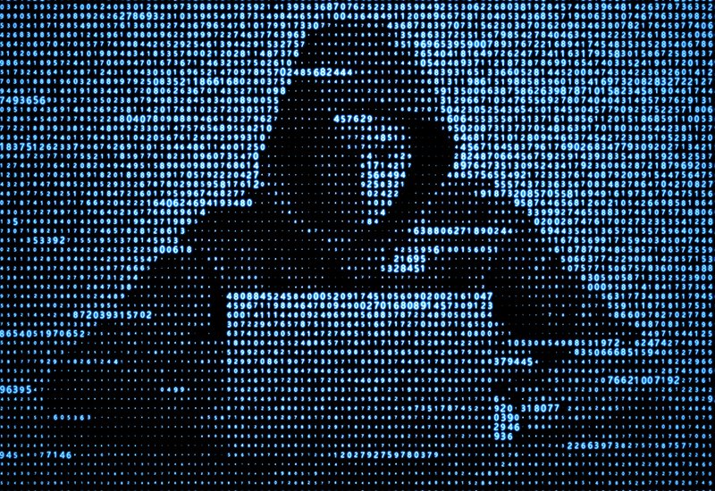 ASCII art image of a hooded figure using a laptop, in blue monospace font on a black background