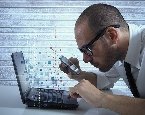 Man closely inspecting laptop with magnifying glass
